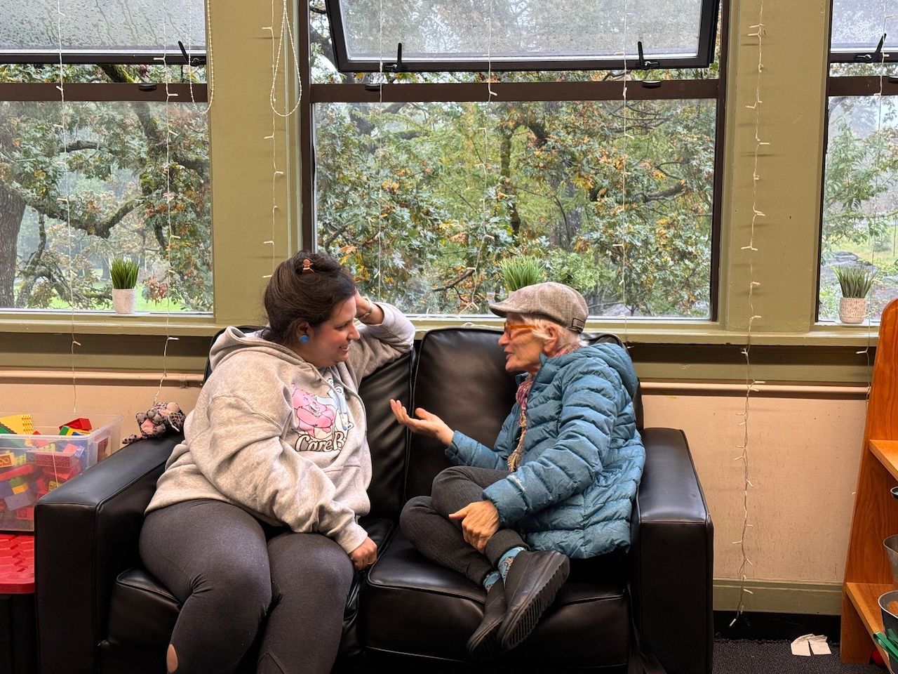 two strangers chatting on a couch beside a window
